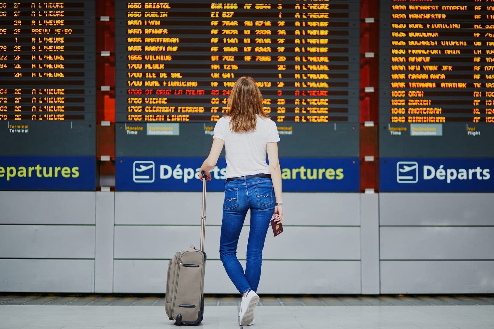 Woman checking a departures board at an airport with a suitcase