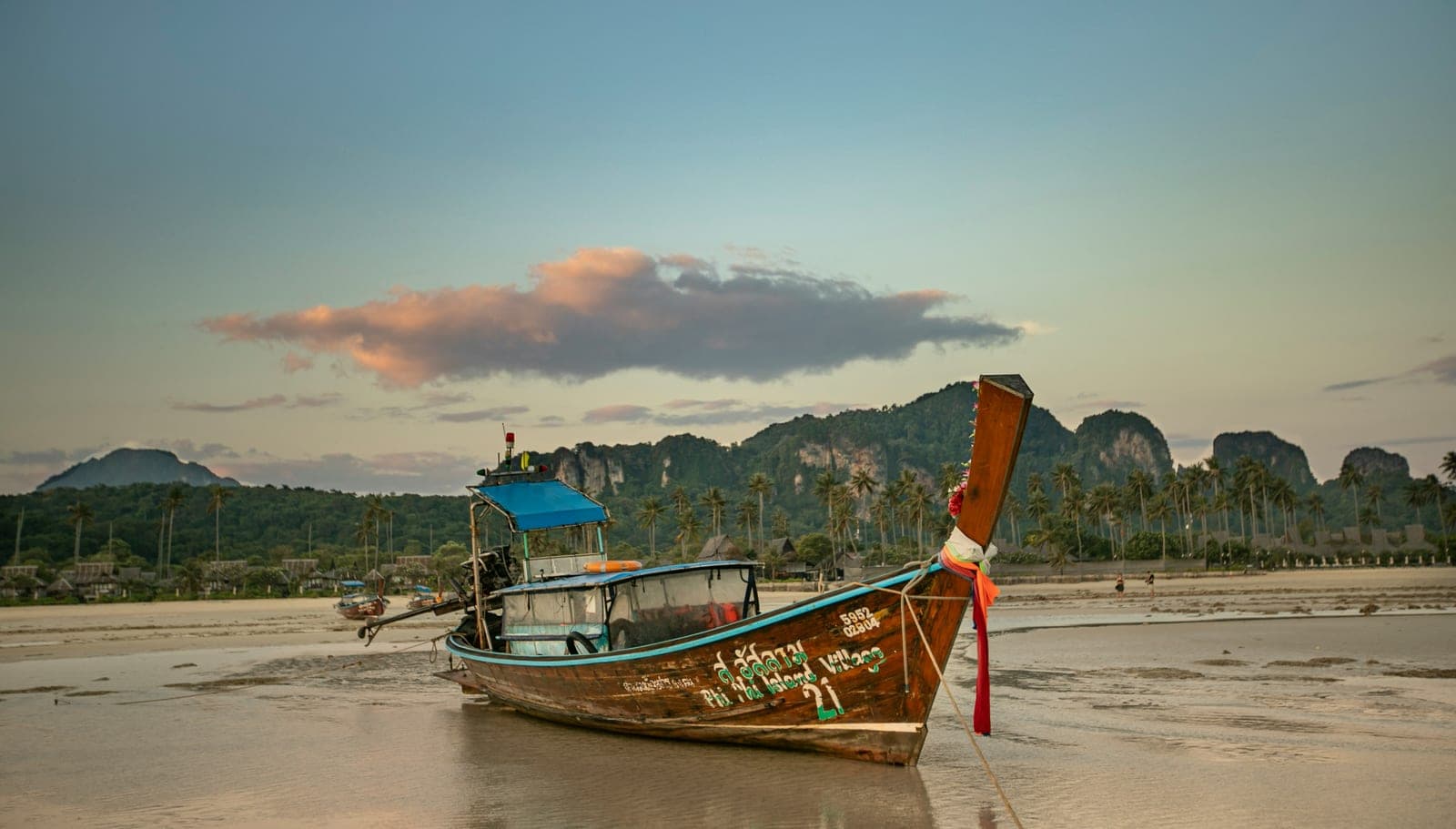 Long-tail boat resting on a tidal beach with limestone cliffs in the distance