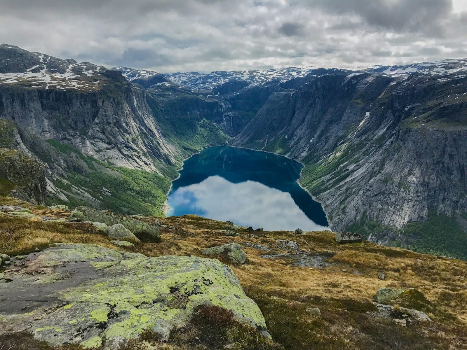 Steep fjord cliffs surrounding a deep blue lake under cloudy skies