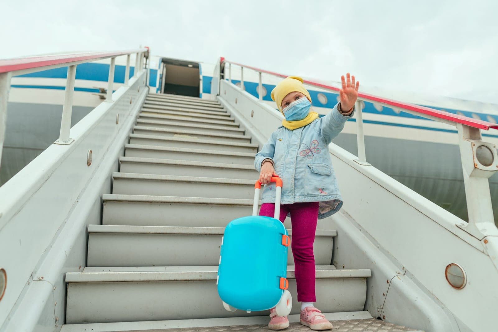 Child boarding an airplane with a blue suitcase
